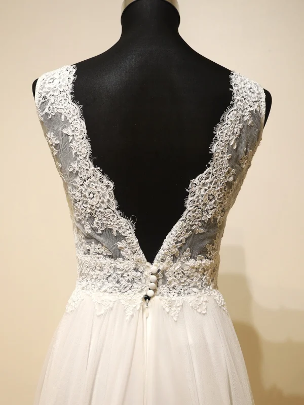 Gros plan sur le dos de la robe de mariée Cachou par Cymbeline, mettant en lumière le travail de dentelle florale sur transparence et la rangée de boutons perlés.