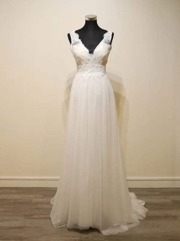 Vue de face de la robe de mariée Cachou signée Cymbeline, présentée sur mannequin dans un showroom, mettant en avant son col en V en dentelle et sa jupe évasée en tulle.