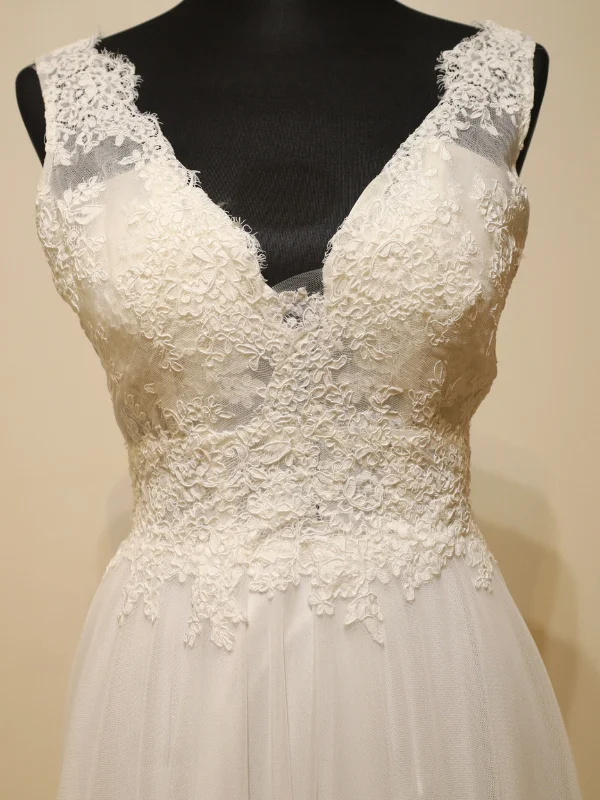 Gros plan sur le bustier de la robe de mariée Cachou par Cymbeline, mettant en valeur son col en V et les motifs délicats de la dentelle rebrodée.