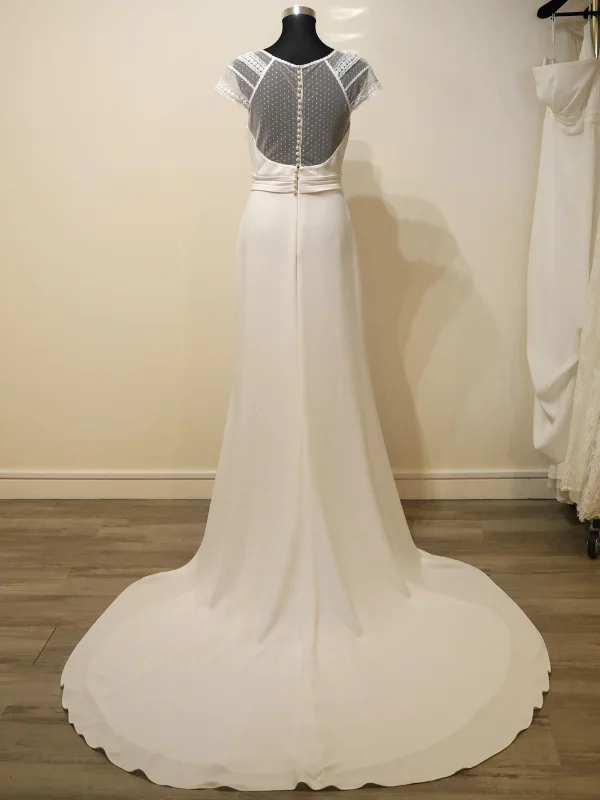 Vue de dos de la robe de mariée Macy par Alma Novia, mettant en avant le bustier en dentelle transparente, la rangée verticale de perles et les délicates manches capelines.