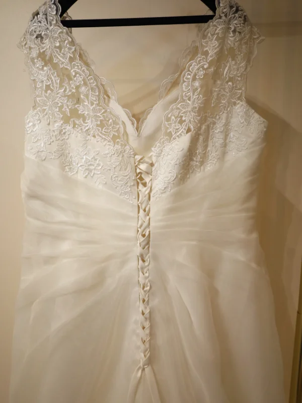 Gros plan sur le système de laçage ajustable au dos d'une robe de mariée grande taille, avec détails de dentelle florale sur les épaules.