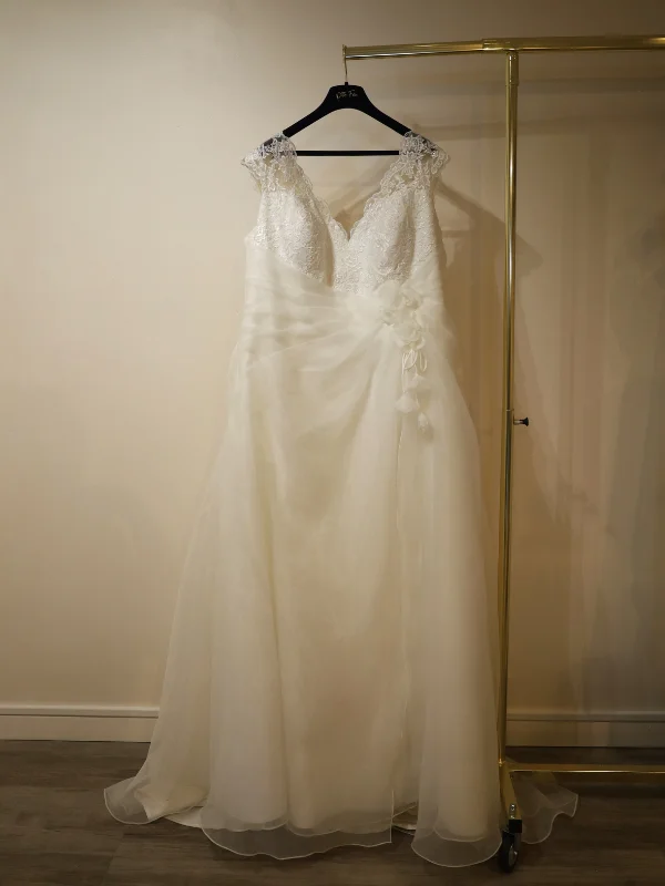Robe de mariée grande taille modèle 23807 par Curvy, présentée de face sur un portant, mettant en valeur son bustier en dentelle et sa jupe évasée en organza.