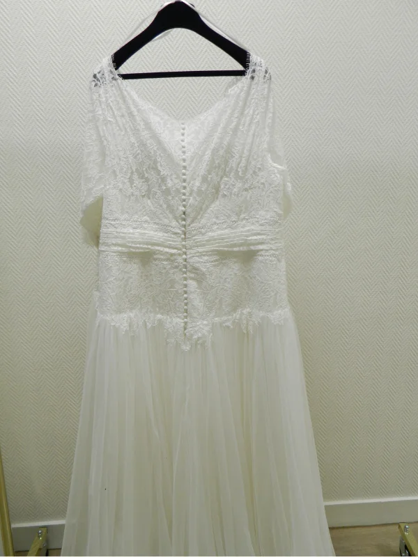 Détail du dos de la robe de mariée grande taille Manon sur cintre, mettant en valeur la rangée de boutons délicats et la dentelle raffinée.