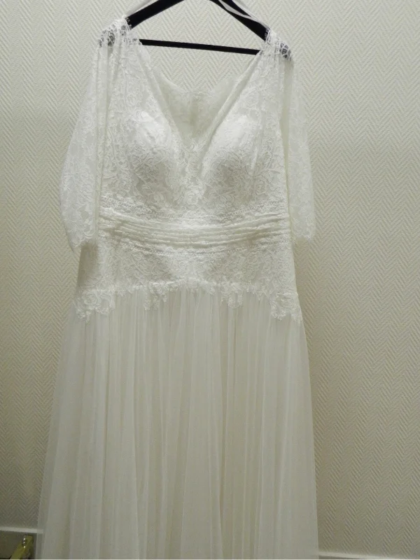 Robe de mariée grande taille modèle Manon présentée sur cintre, mettant en valeur son bustier en dentelle et ses manches mi-longues.