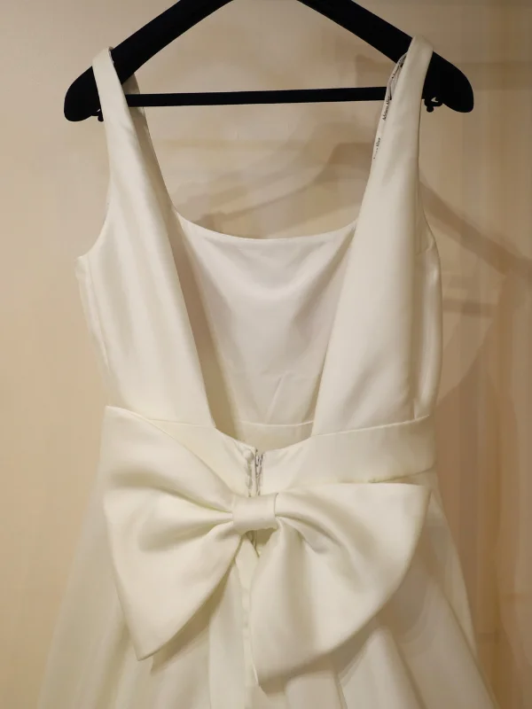 Gros plan sur le dos nu d'une robe de mariée, mettant en avant un élégant nœud papillon en tissu comme détail principal de la fermeture.