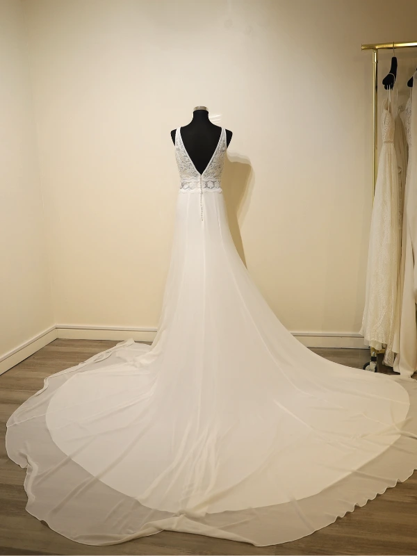 Vue technique de dos de la robe de mariée Luna Novias modèle Fabiola sur mannequin, illustrant le décolleté en V plongeant, le détail des boutons et la traîne étendue.