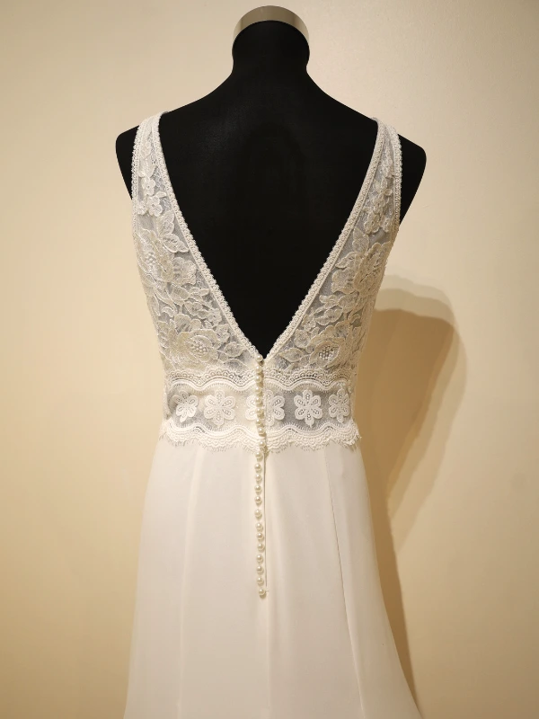 Gros plan sur le dos en V de la robe de mariée Luna Novias modèle Fabiola, montrant la dentelle florale complexes, la ceinture assortie et la rangée de boutons perlés.