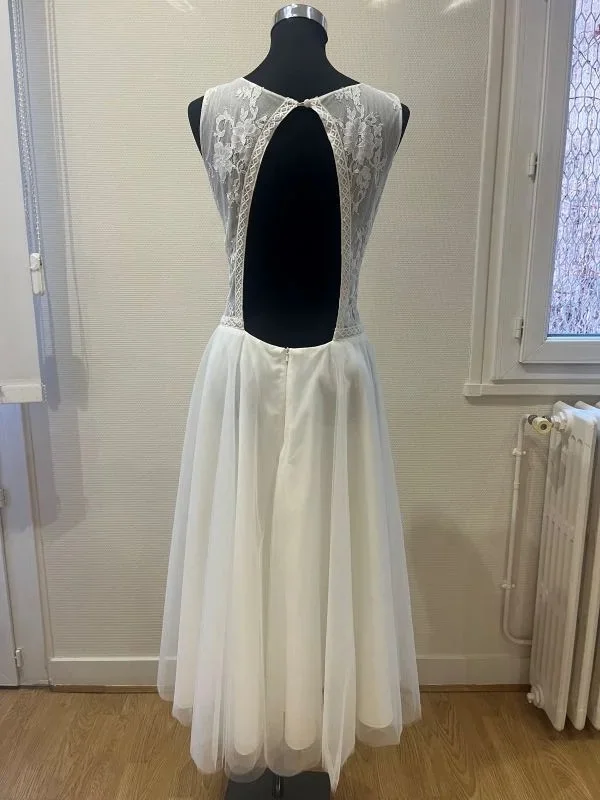 Robe de mariée courte modèle Kasmira par Te Amo en taille 44, vue de dos entière sur mannequin au showroom, montrant le grand décolleté dos nu en losange boutonné à la nuque et la jupe midi en tulle.