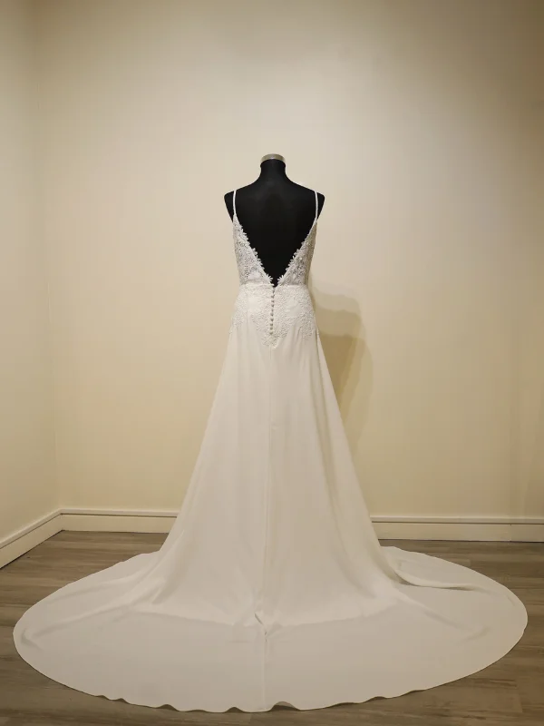"Vue de dos de la robe de mariée minimaliste modèle Levira par Alma Novia, présentée sur portant, mettant en valeur son dos nu profond et sa rangée de boutons élégants."