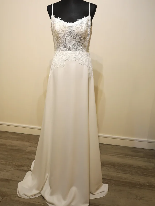 Robe de mariée minimaliste modèle Levira par Alma Novia, présentée de face sur un portant, mettant en valeur son bustier en dentelle et sa jupe épurée en crêpe.