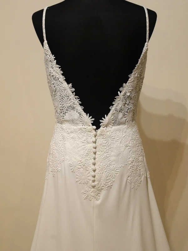 Gros plan sur le dos nu en dentelle de la robe de mariée minimaliste Levira par Alma Novia, montrant les détails de la boutonnière perlée.