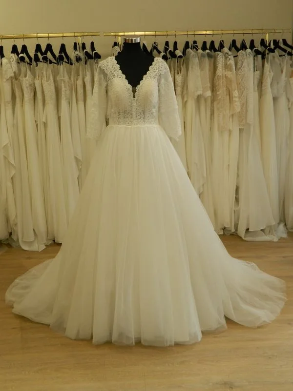 Photo technique de face d'une robe de mariée princesse ivoire sur mannequin dans un showroom, avec bustier en dentelle à manches trois-quarts et décolleté en cœur, et volumineuse jupe en tulle.