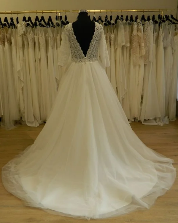 Photo technique de dos complète d'une robe de mariée princesse modèle 23711 par One and Only sur mannequin en boutique, avec grand décolleté en V en dentelle de cils et longue jupe en tulle.
