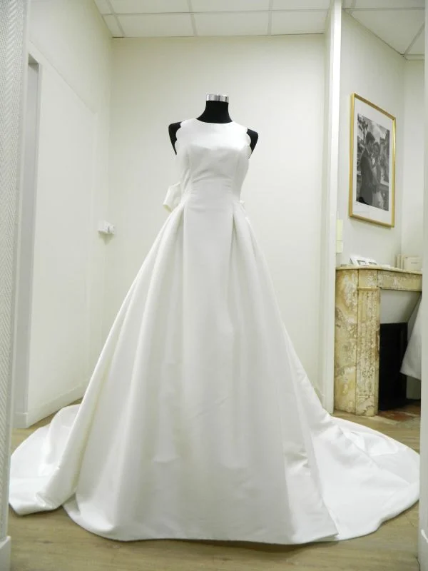 Robe de mariée princesse Evana de Rosa Clará en mikado satiné blanc, avec un bustier col américain aux bords festonnés et une jupe volumineuse à plis creux.