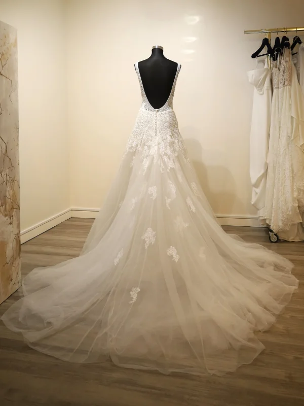 Vue de dos de la robe de mariée princesse modèle Concord par Rosa Clara, présentée sur portant, mettant en valeur son grand décolleté dos nu et sa longue traîne en tulle.