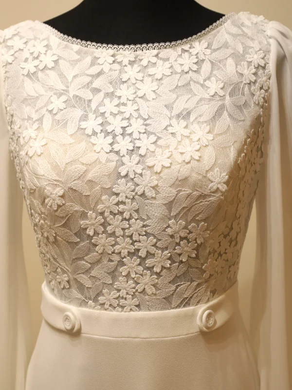 Gros plan sur le bustier en dentelle florale et la ceinture boutonnée du modèle Urim par Rosa Clara, mettant en valeur la précision des détails couture.
