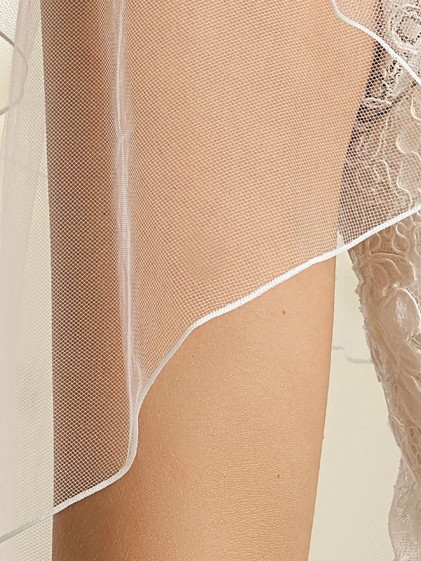 Gros plan sur le tulle souple et la bordure festonnée délicate du voile de mariée Bianco Evento S70