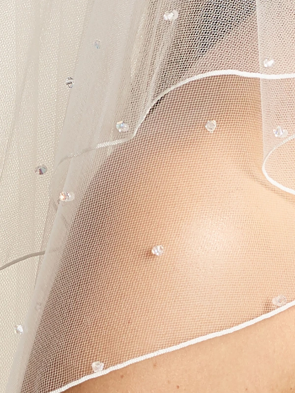 Gros plan sur la bordure festonnée et les perles de verre scintillantes du voile de mariée Bianco Evento S72