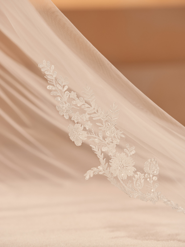Gros plan sur la délicate bordure en dentelle florale ornant le bas du voile de mariée long Bianco Evento S456