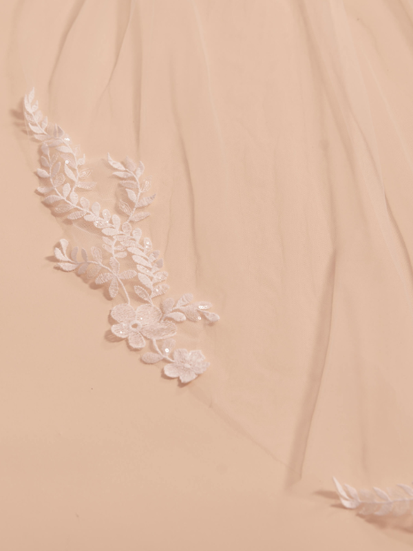 Gros plan détaillé des appliques en dentelle florale et des paillettes scintillantes sur le tulle du voile de mariée Bianco Evento S414