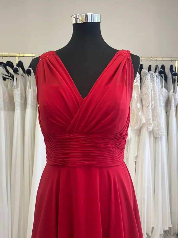 Gros plan sur le bustier drapé d'une élégante robe de cocktail rouge, présentée en showroom, mettant en valeur le travail de couture.