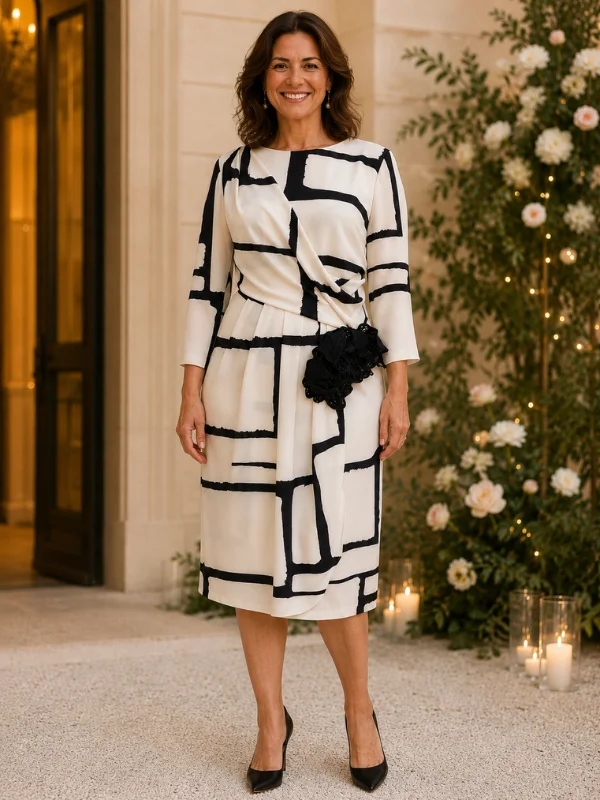 Robe de cocktail Carla Ruiz modèle 196560 blanche et noire avec imprimé géométrique et fleur décorative sur la taille