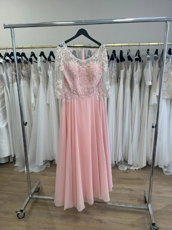 Photo en showroom de la robe de cocktail rose blush NY2819 de Fashion New York suspendue sur un portants de présentation.