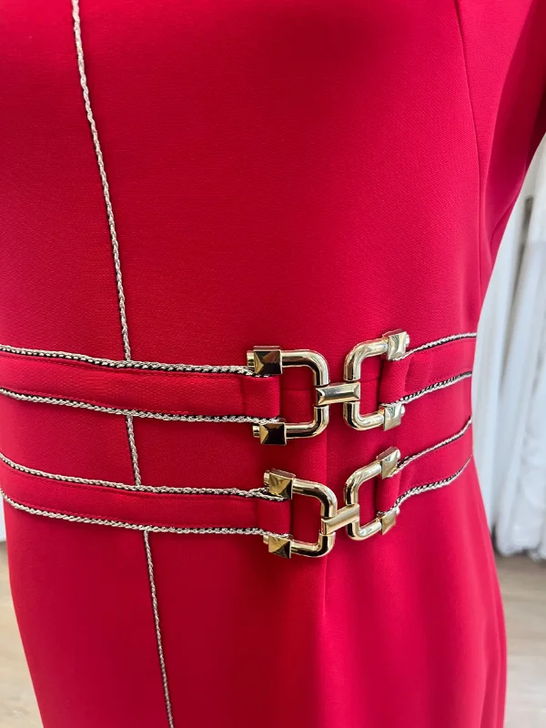 Gros plan sur la taille de la robe de cocktail rouge Carla de Sonia K, montrant la double ceinture ornée de liserés dorés et de fermoirs métalliques dorés, ainsi que le fil doré vertical qui longe la robe.