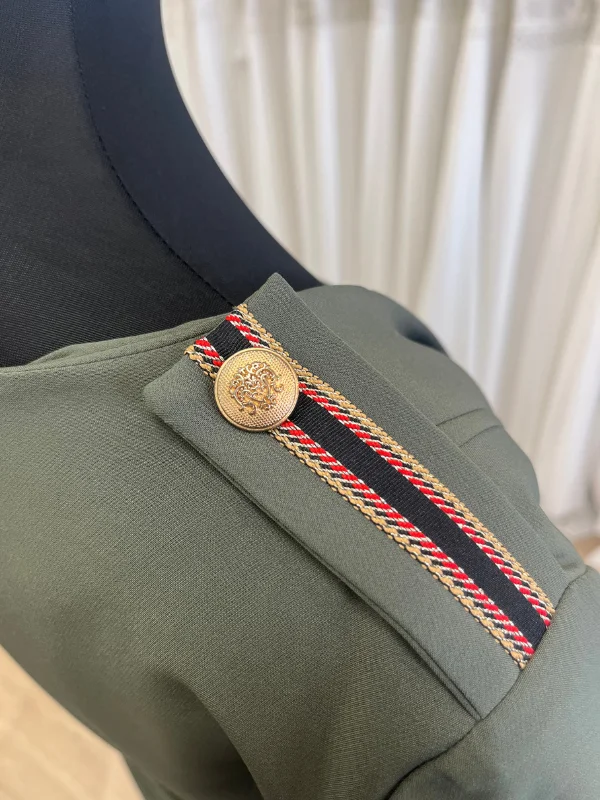 Gros plan sur l'épaule de la robe de cocktail kaki Cupidon de Sonia K, montrant la patte d'épaule ornée d'un galon tressé tricolore noir, rouge et doré, retenue par un bouton doré gravé.