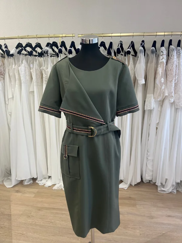 Robe de cocktail kaki Cupidon de Sonia K présentée de face sur un buste mannequin dans la boutique Petite Folie. La tenue intègre un revers drapé asymétrique bordé d'un galon rayé, une ceinture avec boucle dorée et une poche plaquée zippée sur la jupe.